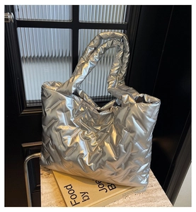 Detail of silver quilted tote bag with padded handles and metallic finish on textured surface