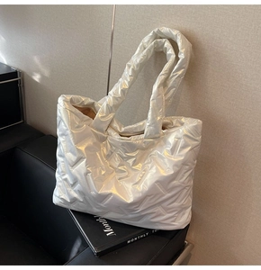 Detailed view of white quilted tote bag with soft padded straps on a leather bench