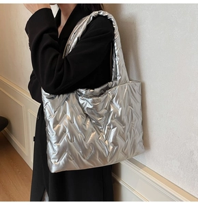 Close-up of a silver puffer tote bag with quilted metallic finish on model's shoulder