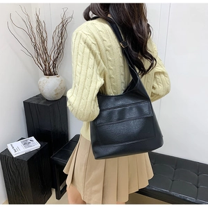 Close-up of a black textured faux leather tote bag with large front pocket on a model