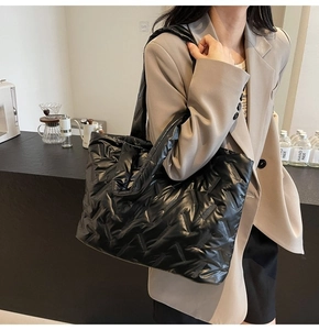 Detailed close-up of high-gloss quilted black puffer tote bag texture and nylon stitching