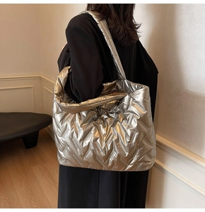 Model wearing a large silver metallic quilted tote bag over shoulder with black coat