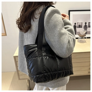 Gros plan sur le sac fourre-tout matelassé noir en nylon brillant porté par un modèle