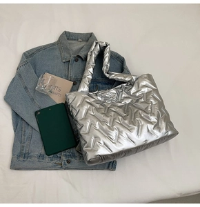 Flat lay of a large silver puffer tote bag with quilted texture and metallic finish