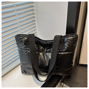 Nahaufnahme der schwarzen gesteppten Puffer-Tasche mit breiten Stoffträgern bei Tageslicht