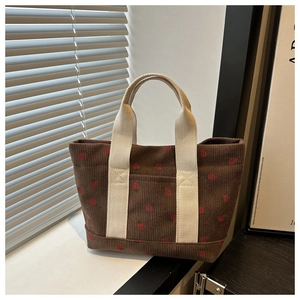 Detailed texture of dark brown corduroy tote bag featuring red strawberry print and cream handle