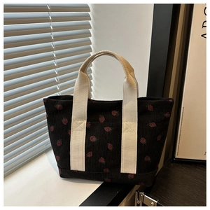 Detail of black corduroy bucket bag featuring red strawberry patterns and wide cream handles