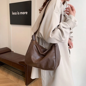Braune Leder-Hobo-Tasche für Damen mit breitem Gurt, getragen zum beigen Trenchcoat