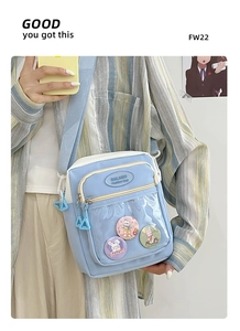 Detail of light blue crossbody ita bag featuring clear front window with cartoon badges