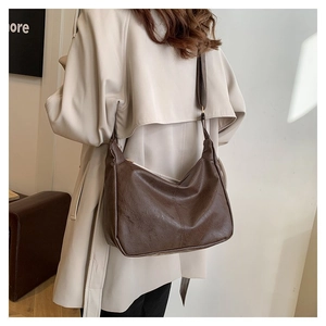 Detail der braunen PU-Leder-Hobo-Tasche mit breitem Gurt zu einem beigen Trenchcoat