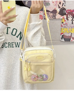 Detail of yellow nylon ita bag with transparent front pocket and cute cartoon badges