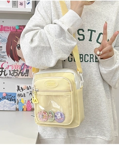 Detail of yellow and white crossbody bag with clear window and cartoon pins