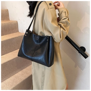 Detail of black faux leather tote bag with metallic studs and magnetic closure on model