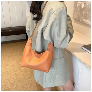 Texture détaillée d'un sac hobo en cuir orange porté à l'épaule pour femme
