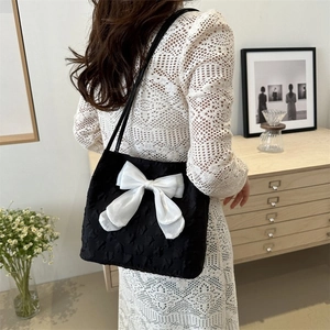 Detail view of black textured fabric tote bag with a white satin bow decoration