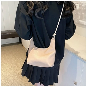 Detail of a beige crescent crossbody bag with knotted shoulder strap worn by a model