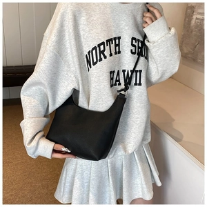 Detalle de un bolso hobo de media luna negro minimalista llevado por una modelo casual