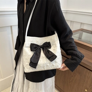 Detail of white tote bag featuring embossed texture and a large black silk bow decoration
