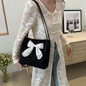 Detail of black heart-textured fabric tote bag featuring a large white silk-finish bow