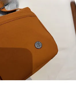 Détail du tissu en nylon imperméable et logo M en métal sur sac bandoulière marron