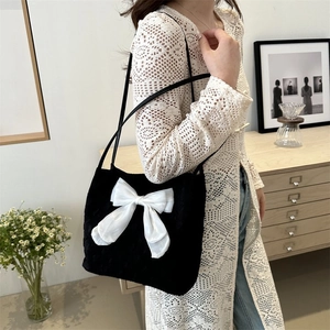 Detail of elegant black velvet tote bag with a large white satin bow and slim strap