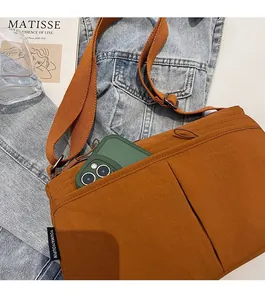 Détail du sac bandoulière en nylon caramel avec poche zippée sur du denim
