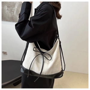 Detail of minimalist cream canvas tote bag with black leather trim and bow accent