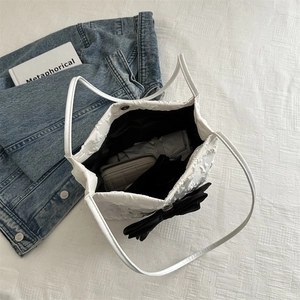 Detail of white pleated tote bag featuring black bow decoration and spacious interior