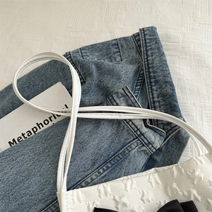 Close-up of white leather tote with star-embossed texture and black satin bow detail