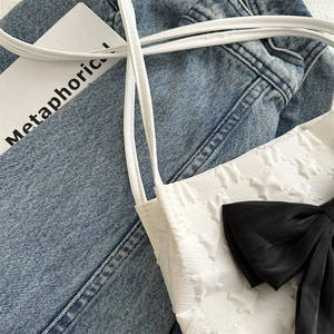 Close-up of white tote bag with embossed star texture and large black ribbon bow detail