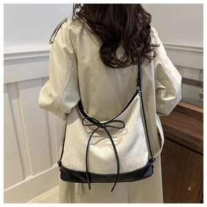 Detailed close-up of a minimalist canvas tote bag with black leather trim and bow knot