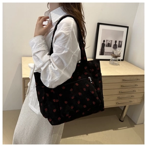 Dettaglio della stampa fragola sulla borsa tote in velluto nero indossata da una modella