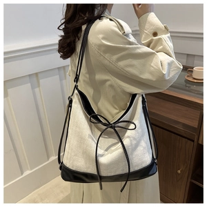 Close-up of minimalist canvas tote with black leather straps and decorative bow detail