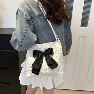 White quilted tote bag with large black bow decoration worn on model's shoulder