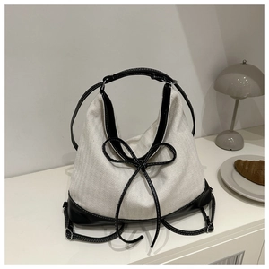Detailed close-up of cream canvas tote bag with black leather trim and decorative bow knot