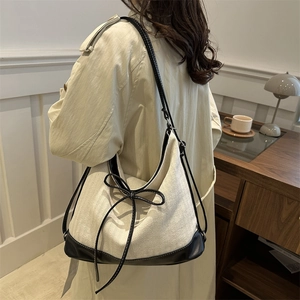 Chic beige canvas and black leather shoulder bag with bow detail on a stylish model