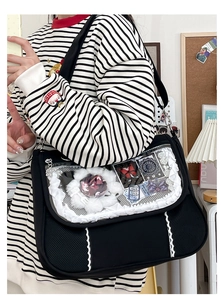 Detail of black ita bag with clear window, white lace trim, and decorative plush accessories