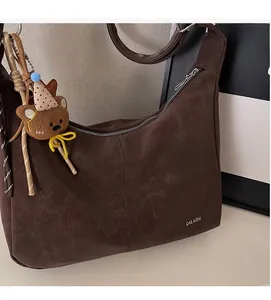 Détail d'un sac sous le bras en cuir marron vintage avec un porte-clé ours en peluche