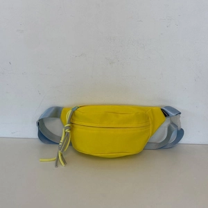 Detail der gelben Bauchtasche mit blauem Webband und Modelabel auf schlichtem Grund