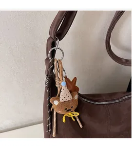Détail d'un charme d'ours en peluche avec chapeau de fête et cordons sur un sac en cuir
