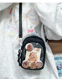 Detail of a black ita bag with transparent PVC window showing cute capybara badges