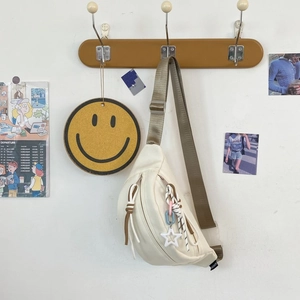 Detailansicht der cremeweißen Canvas-Brusttasche mit braunem Gurt und Sternanhänger