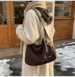Sac hobo en daim marron avec charme ours porté sur un manteau d'hiver blanc