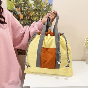 Detail of yellow and orange drawstring tote bag with striped cords and grey handle