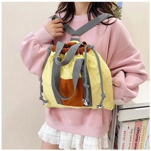 Detail showing a yellow drawstring backpack with orange pocket worn over one shoulder by a model