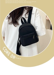 Detail shot of black nylon mini backpack featuring brand label and zip pocket
