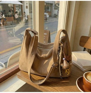 Vue détaillée du sac cabas en daim marron foncé avec pendentif ours sur table en bois