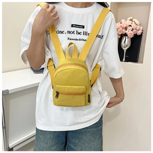 Detail view of bright yellow mini nylon backpack worn by a model in casual setting