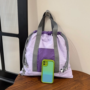 Detail view of purple nylon drawstring bag with color-block pockets and woven handles