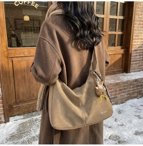 Détail du sac hobo en daim kaki avec pendentif ours sur un mannequin dans la rue enneigée